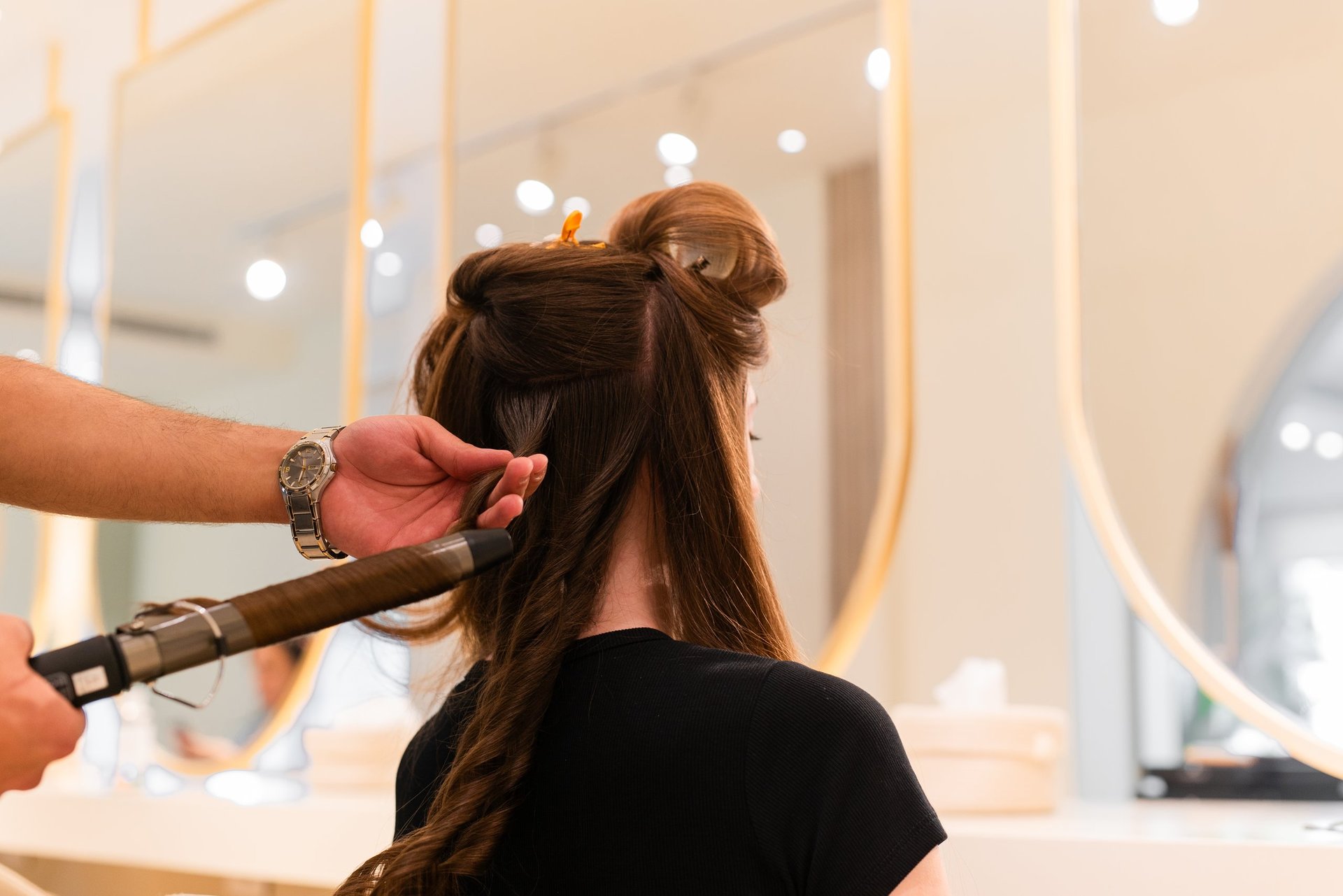 Hairstylist curling long brown hair with heated curling iron