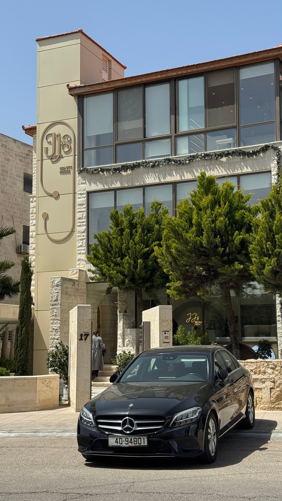 Black Mercedes-Benz car parked in front of a modern beige and brick building with large windows and green plants